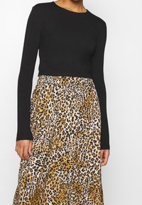 Černý top s dlouhým rukávem v kombinaci s leopardím vzorem sukně v odstínech béžové, černé a bílé, se elastickým pasem a volným střihem.
