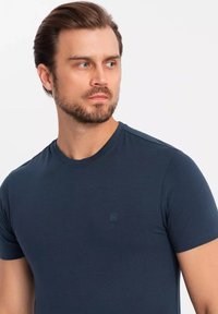Granatowa bawełniana koszulka z krótkimi rękawami, okrągłym dekoltem i subtelnym logo na piersi. Gładka tekstura i dopasowany krój.
