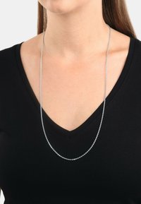 Silver kedja halsband med en delikat design, som har tv å lager av strängar som vilar graciöst på en svart v-ringad topp.