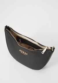 Borsa in sintetico nera con design curvo, chiusura con zip dorata e logo del marchio sul fronte. L'interno presenta multiple tasche.