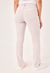 Helle rosa Slim-Fit-Jeans mit Gesäßtaschen, glatter Textur und subtilen Nähten. Kombiniert mit weißen Sneakers.