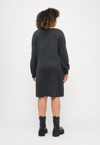 Gray, knitted sweater dress with long sleeves, a round neckline, and a straight cut, paired with black ankle boots featuring thick soles.