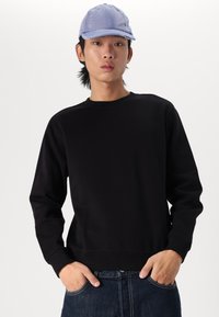 Sudadera negra de manga larga y diseño de cuello redondo, combinada con una gorra azul clara que presenta detalles bordados y un visera curvada.