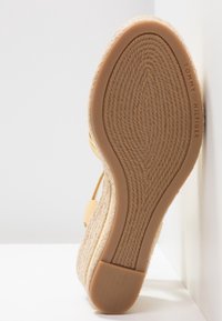 Semelle de sandale compensée espadrille beige avec texture en corde et talon en caoutchouc, nom de la marque Tommy Hilfiger embossé sur le côté.