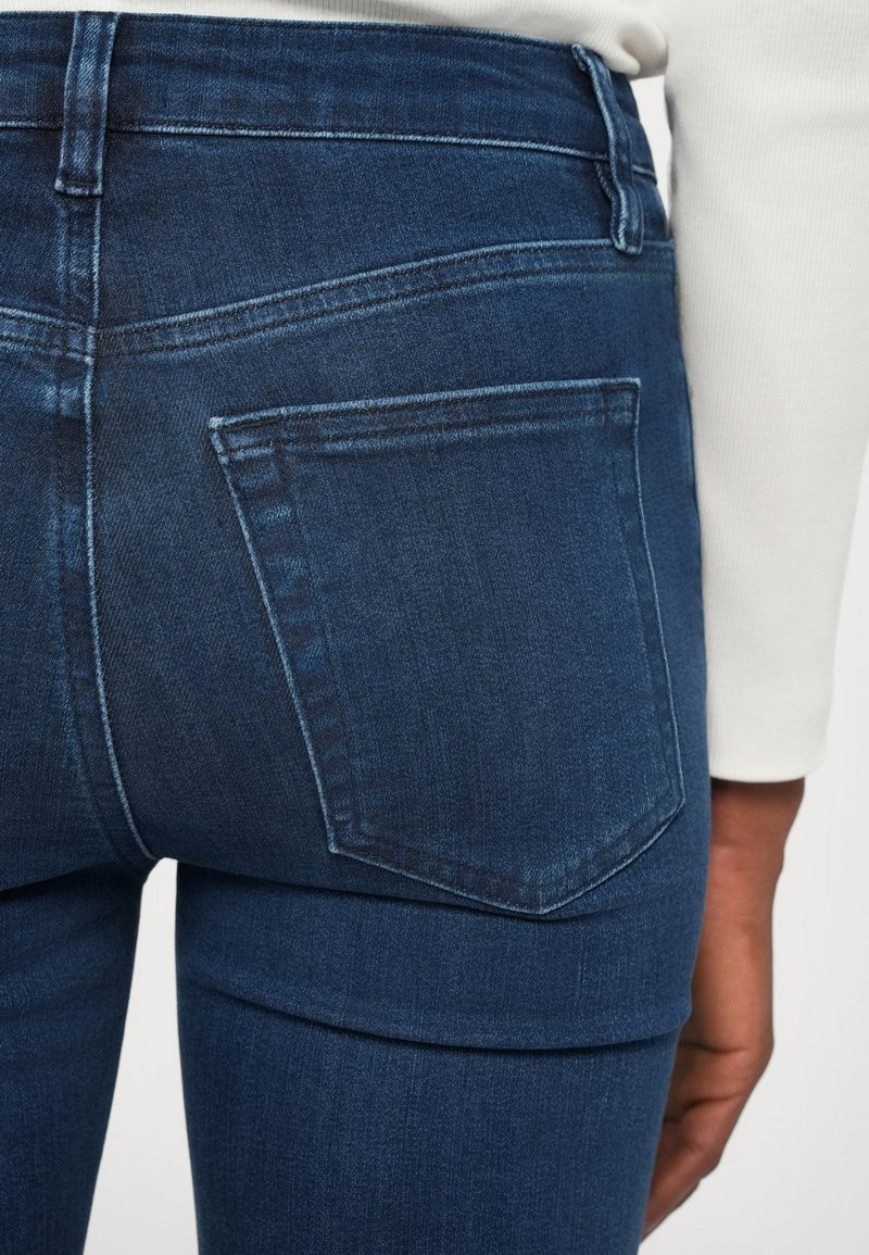 Dark blue denim jeans with a close-fitting design. Features a back pocket with a subtle stitching pattern and a smooth texture.