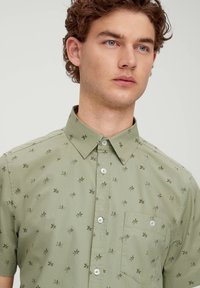 Kurzarm, hellgrünes Hemd mit Blumenmuster, mit Knopfkragen, Brusttasche und weißen Knöpfen. Glatte Textur.