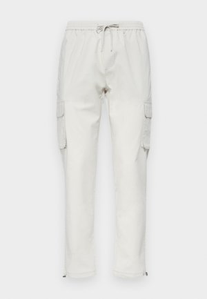 Světlé béžové cargo kalhoty vyrobené z bavlny, s elastickým pasem a stahovací šňůrkou, s bočními kapsami a zipy na kotnících.