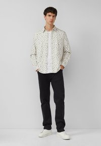 Biała koszula na guziki z drobnym niebiesko-zielonym kwiatowym wzorem, noszona na białej koszulce, w połączeniu z czarnymi spodniami i białymi trampkami.