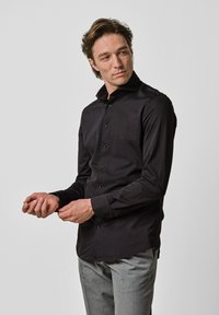 Zwarte blouse met lange mouwen en een button-down kraag, fitted ontwerp en een gladde textuur, gecombineerd met lichtgrijze broek.