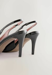 Czarne lakierowane sandały na wysokim obcasie z noskiem w szpic, z paskami wokół kostki, a wewnątrz różowa podszewka. Eleganckie, smukłe obcasy.