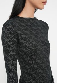 Donna che indossa un top a maniche lunghe nero con un motivo geometrico e floreale a pois bianchi ripetuto.