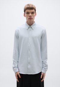 Svetlomodrá košeľa s dlhými rukávmi na gombíky, s textúrovanou látkou, klasickým golierom a jemnou výšivkou na hrudi. Dizajn s úzkym strihom.