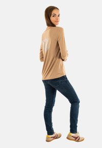 Beige lange mouwen shirt met een reflecterend sterontwerp op de achterkant, gecombineerd met donkerblauwe strakke jeans en meerkleurige sneakers.