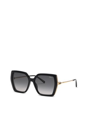 Lunettes de soleil noires surdimensionnées de forme carrée avec branches en métal doré et verres dégradés foncés, vue en angle sur fond blanc.