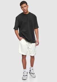 Sort oversized t-shirt med korte ærmer, parret med hvide shorts. Shortsene har en kantdetalje, mens outfittet afsluttes med træningssko.