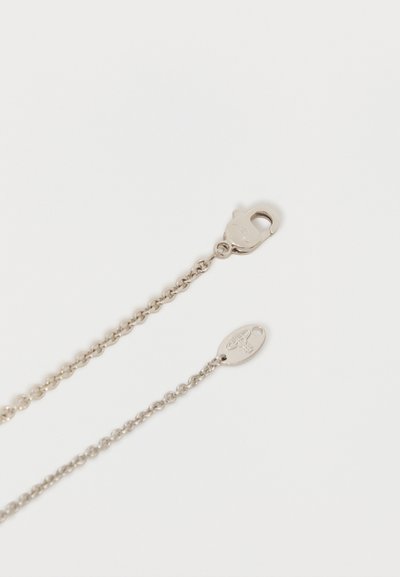 Collier chaîne de couleur argent avec un fermoir en forme de homard et une étiquette ovale gravée d'un petit logo sur un fond blanc.