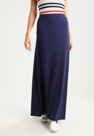 Marineblauwe maxi-rok van lichtgewicht stof met een elastische tailleband. Draagt wit espadrilles met een gladde textuur en eenvoudig ontwerp.