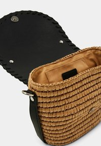 Tkaná hnědá slámová taška s černým koženým klopou. Obsahuje magnetické zavírání, vnitřní kapsu a texturovaný design se zaobleným tvarem.