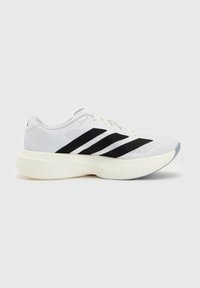 Chaussure de sport blanche avec des bandes noires et semelle blanche épaisse, vue de côté sur un fond gris clair uni.