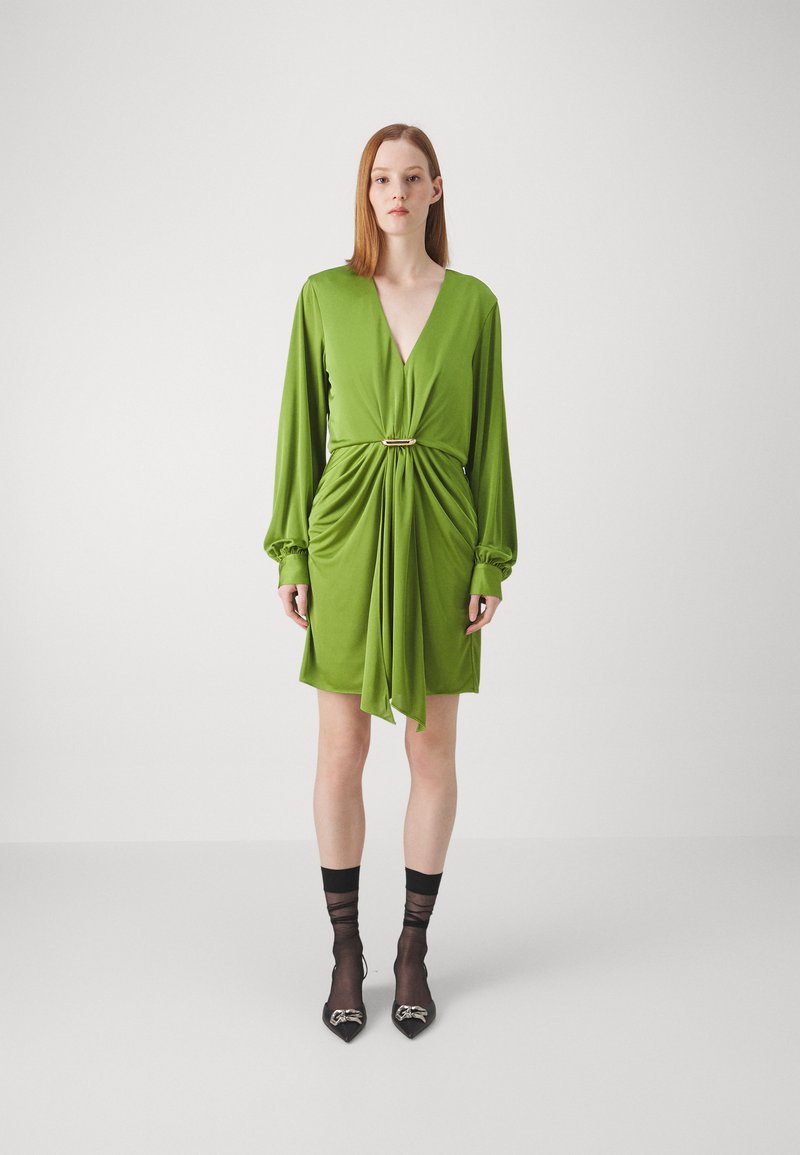 Rochie verde înfoiată cu mâneci lungi, decolteu adânc în V, detaliu cu talie plisată și un accent auriu. Modelul a asortat-o cu pantofi negri cu vârful ascuțit.