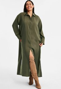 Olivgrünes, knopfbares Hemdkleid mit langen Ärmeln, seitlichen Schlitzen und einem lockeren Schnitt aus leichtem Stoff. Mit einem Kragen akzentuiert.