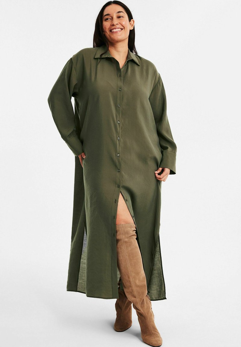 Olivgrünes, knopfbares Hemdkleid mit langen Ärmeln, seitlichen Schlitzen und einem lockeren Schnitt aus leichtem Stoff. Mit einem Kragen akzentuiert.
