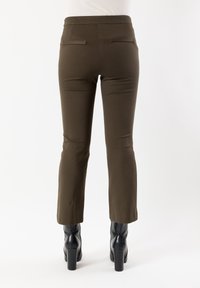 Pantaloni marroni aderenti con una texture liscia, vita media, leggero svasato all'orlo e due tasche posteriori. Indossati con stivali neri con tacco.