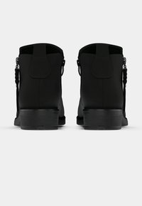 Melnas potīšu zābaki ar gludu apdari, nelielu bloka papēdi, cilpiņu vilkšanai un pītas detaļas sānos.