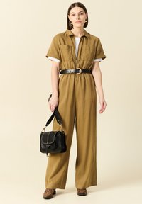Mono verde oliva con cinturón, mangas cortas, dos bolsillos en el pecho y piernas anchas. Combinado con un bolso negro con detalles de tachuelas.