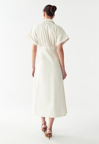 Kreemivalge, põlve pikkune kleit lühikeste varrukatega, elastse vöökohtadega ja külgmürad. Valmistatud siledast kangast, millel on krae.