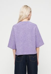 Pull en maille lavande à manches courtes, coupe décontractée et col rond, associé à un jean large bleu foncé. Texture douce visible.