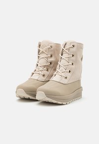 Beige vanntette ankelstøvler med overdel i semsket skinn og stoff, rund tå, snøring foran og strukturert gummisåle. Har metalløyer og sømmer.