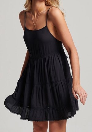 Black, sleeveless sundress with a tiered design and ruffled hemline. Made of lightweight fabric, featuring thin straps and a loose fit.