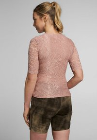 Rosa Spitzenoberteil mit kurzen Ärmeln, das ein florales Muster und gewellte Kanten aufweist, kombiniert mit braunen Shorts mit einer weichen, strukturierten Oberfläche.
