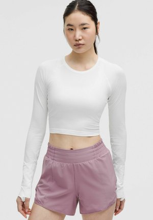 Weißes Langarm-Crop-Top mit gerippter Textur, kombiniert mit hellrosa Shorts mit elastischem Bund und abgerundetem Saum.