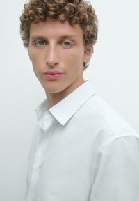 Witte button-up overhemd met een spread collar, vervaardigd uit een gladde stof. Kenmerkt zich door een subtiele textuur en een afgeronde zoom. Slank model.