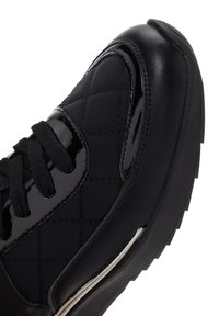 Sneaker nera con tomaia in tessuto trapuntato, dettagli in vernice lucida, lacci neri e suola in gomma texture con un dettaglio argento.