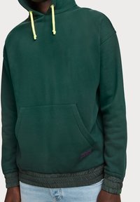 Sudadera verde con un acabado texturizado, cordones de contraste en amarillo neón, bolsillo tipo canguro y dobladillos y puños elásticos.