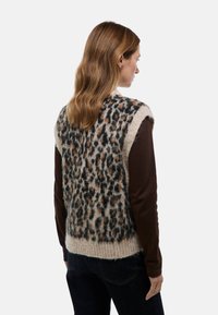 Gilet tricoté en imprimé léopard avec une texture douce et duveteuse, doté d'un devant beige et d'accents noir-brun, porté sur une chemise à manches longues marron.