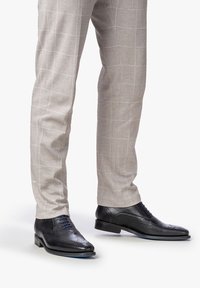 Scarpe da dress in pelle nera con dettagli brogue, lacci e una finitura lucida, abbinate a pantaloni a scacchi grigio chiaro.