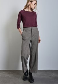 Marlow-punainen pitkähiha neule yhdistetty korkeavyötäröisiin ruudullisiin leveälahkeisiin housuihin. Mustat nilkkurit täydentävät asua. Yksinkertainen, siisti muotoilu.