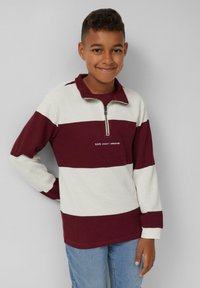 Langärmliger Pullover in Maroon und cremefarbenen Streifen. Aus Baumwolle gefertigt, mit einem Viertel-Reißverschluss-Kragen und gesticktem Logo auf der Brust.