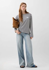 Striped long-sleeve shirt in navy and white, paired with light blue wide-leg jeans. Brown suede bag and blue slide sandals complete the look.