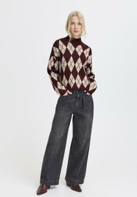 Maglione a motivo argyle marrone e crema con collo alto, abbinato a jeans scuri a gamba larga e stivaletti con tacco marroni.