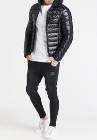 Sort dunjakke med hætte, med quiltet design og lynlås foran. Kombineret med sorte skinny jeans og hvide sneakers.