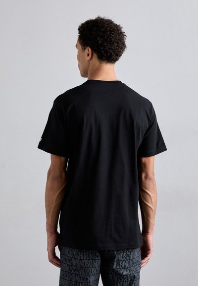 T-shirt noir à manches courtes en coton, avec un col rond. Le dos est uni sans logos, associé à un pantalon à motifs.
