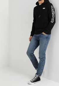 Svart luvtröja med framficka och vitt "Levi's"-logotyp, kombinerad med ljusblå jeans och svarta höga sneakers.