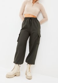 Pantalones cargo verde oliva con bolsillos laterales, cintura elástica y un ajuste relajado, combinados con botas de cordones de tacón grueso en color beige.