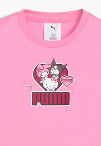 Różowa koszulka z logo PUMA i postaciami Hello Kitty oraz jej przyjaciół w grafikę w kształcie serca na obszarze klatki piersiowej.