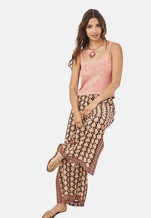 Top de tirantes de punto rosa combinado con pantalones anchos de diseño estampado con flores y una cinturilla decorativa. Sandalias con tiras complementan el conjunto.